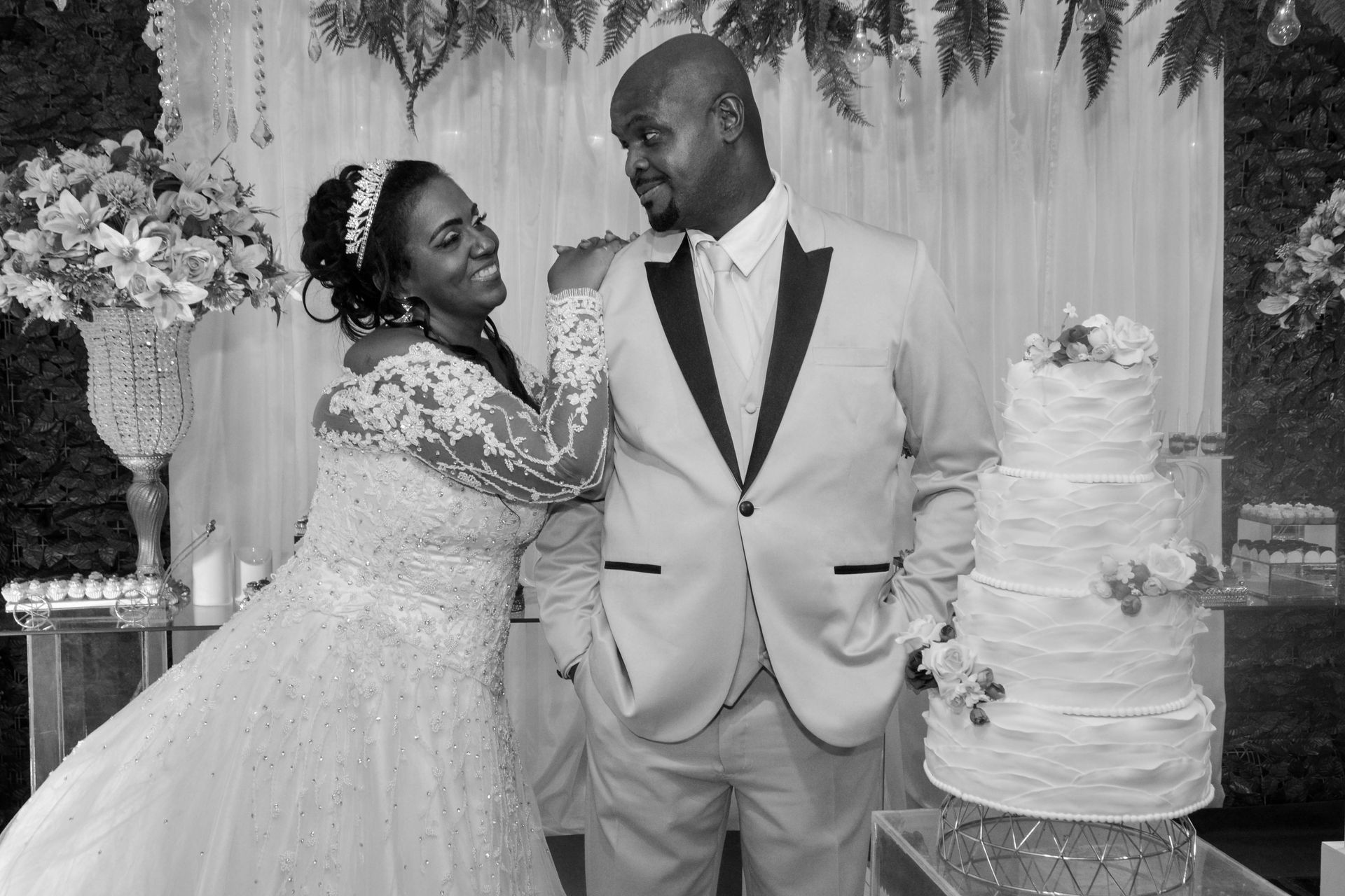 Noivos posam perto de um bolo de vários andares na recepção do casamento.