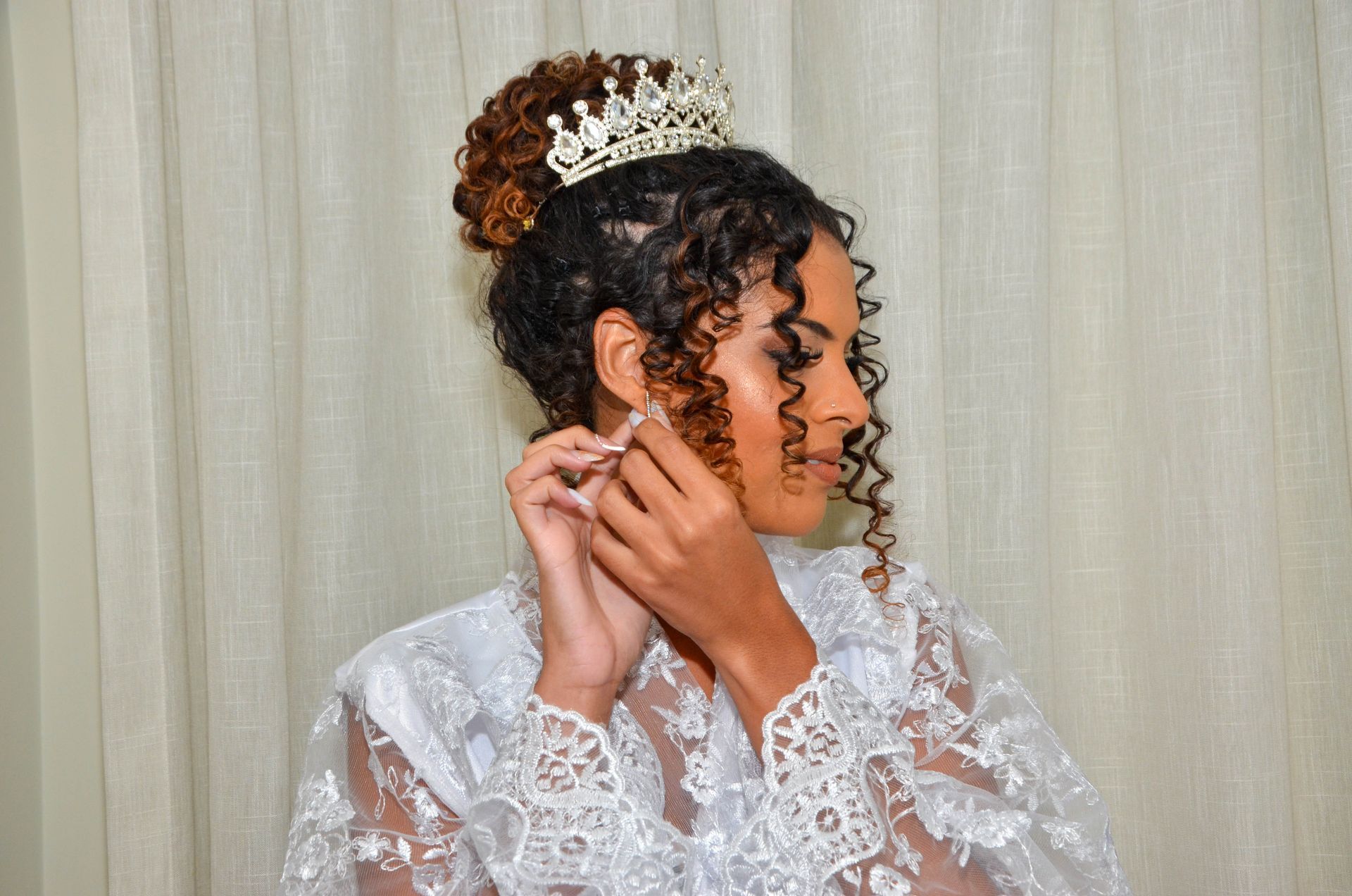 Mulher com túnica de renda branca, usando coroa, brincos e cabelo preso.
