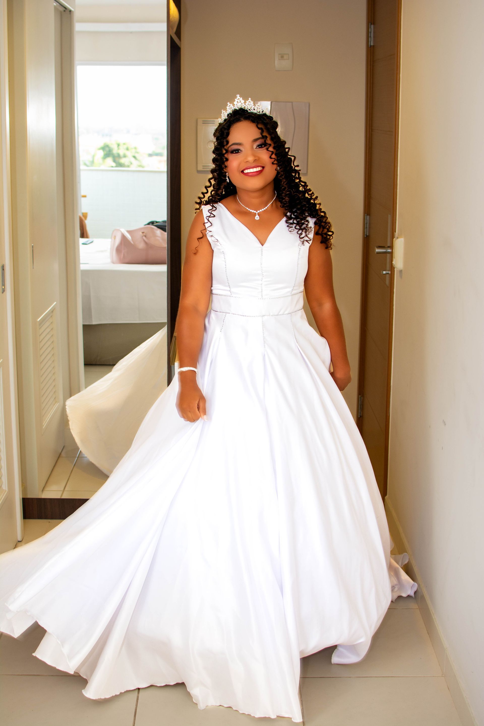 Noiva em vestido de noiva branco sorri, parada na porta.