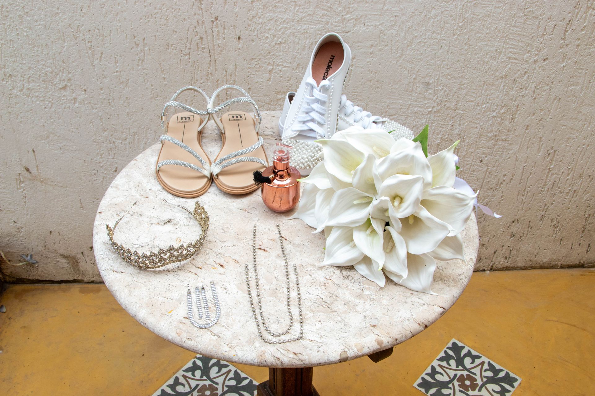 Acessórios de casamento em uma mesa redonda: sandálias, tênis, joias, buquê e elementos decorativos.