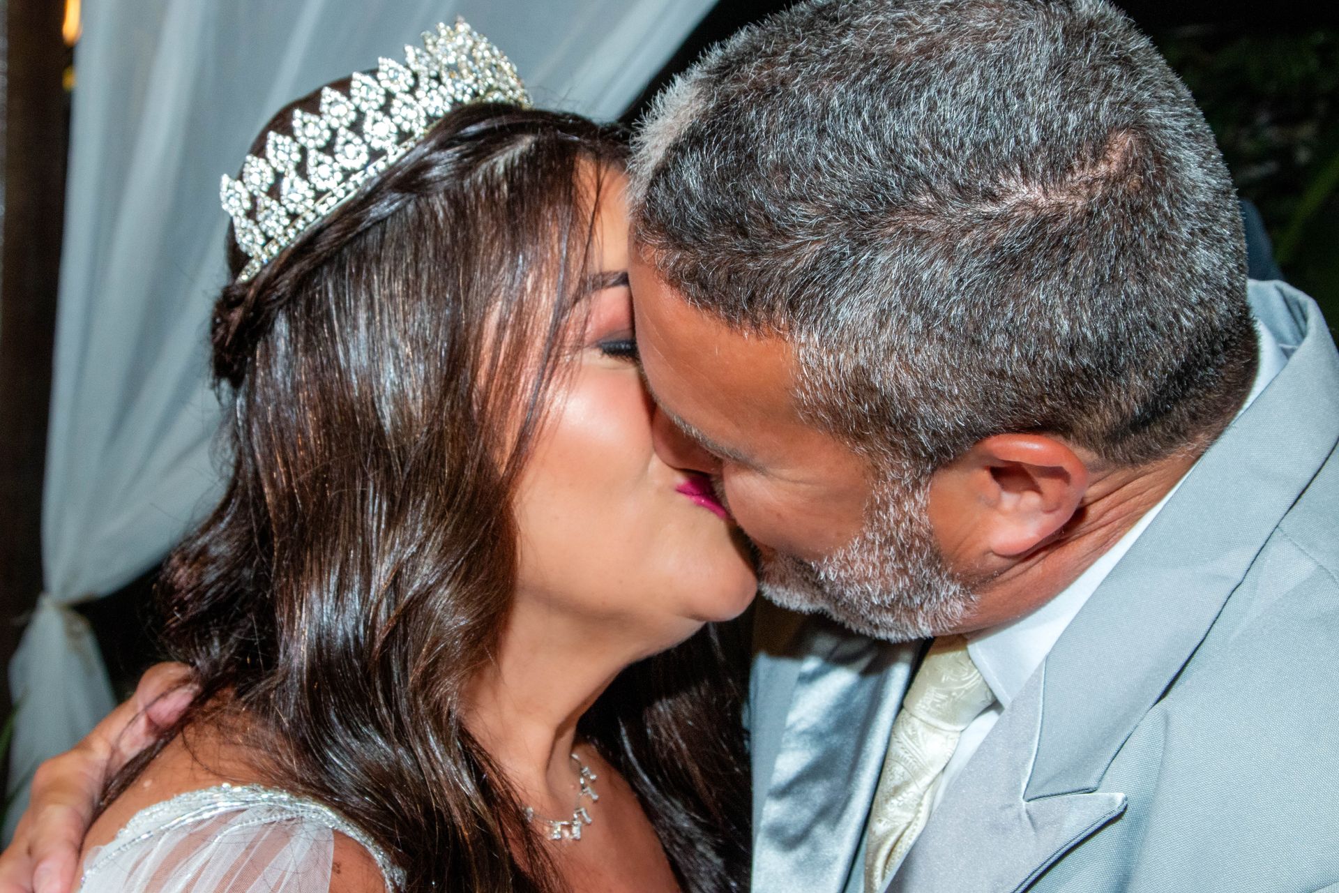 Casal se beijando em um casamento; mulher de tiara, homem de terno.