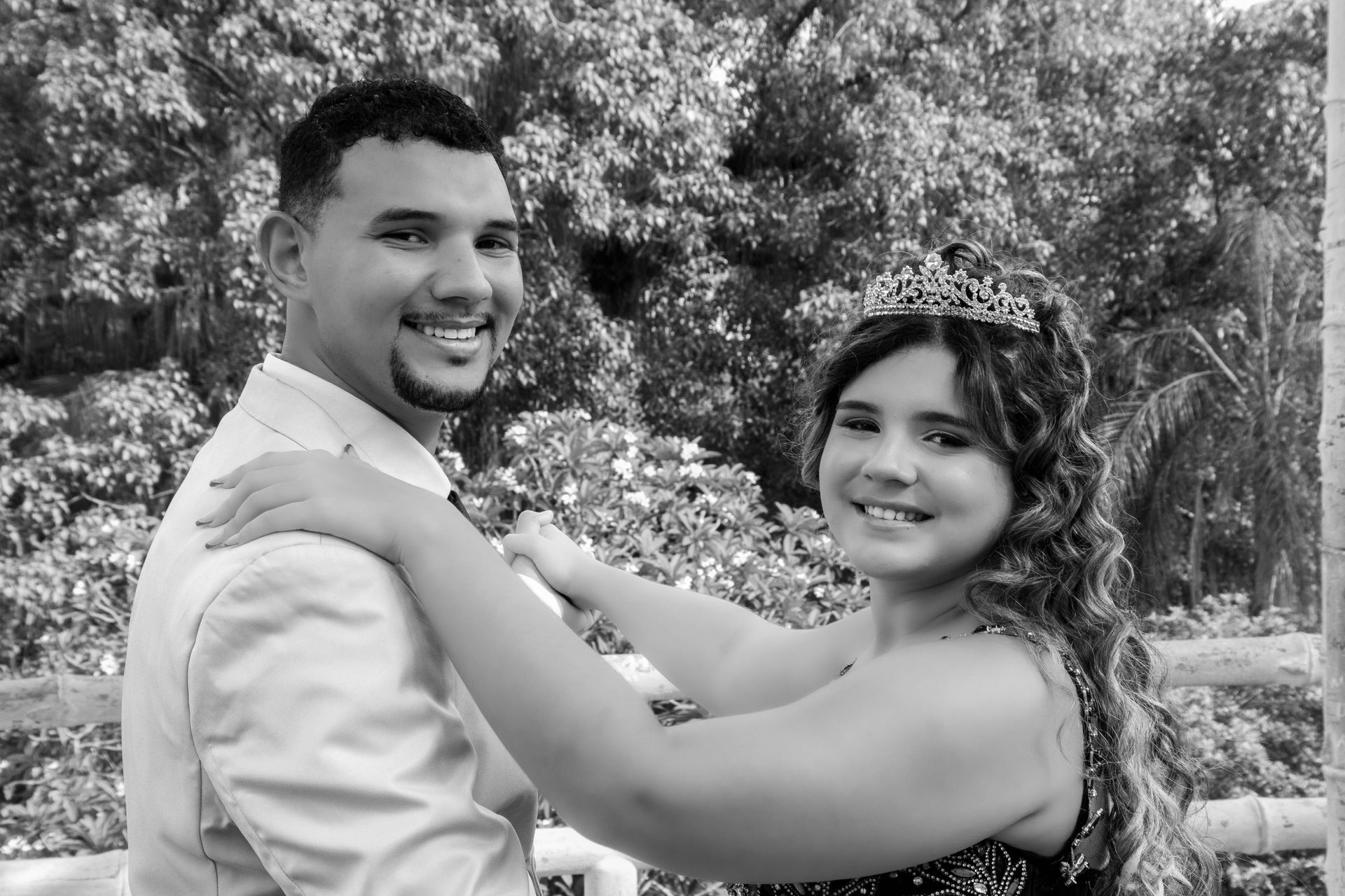 Homem e mulher sorrindo, ao ar livre. Mulher de tiara, braços erguidos como se estivesse dançando, homem com o braço em volta dela.