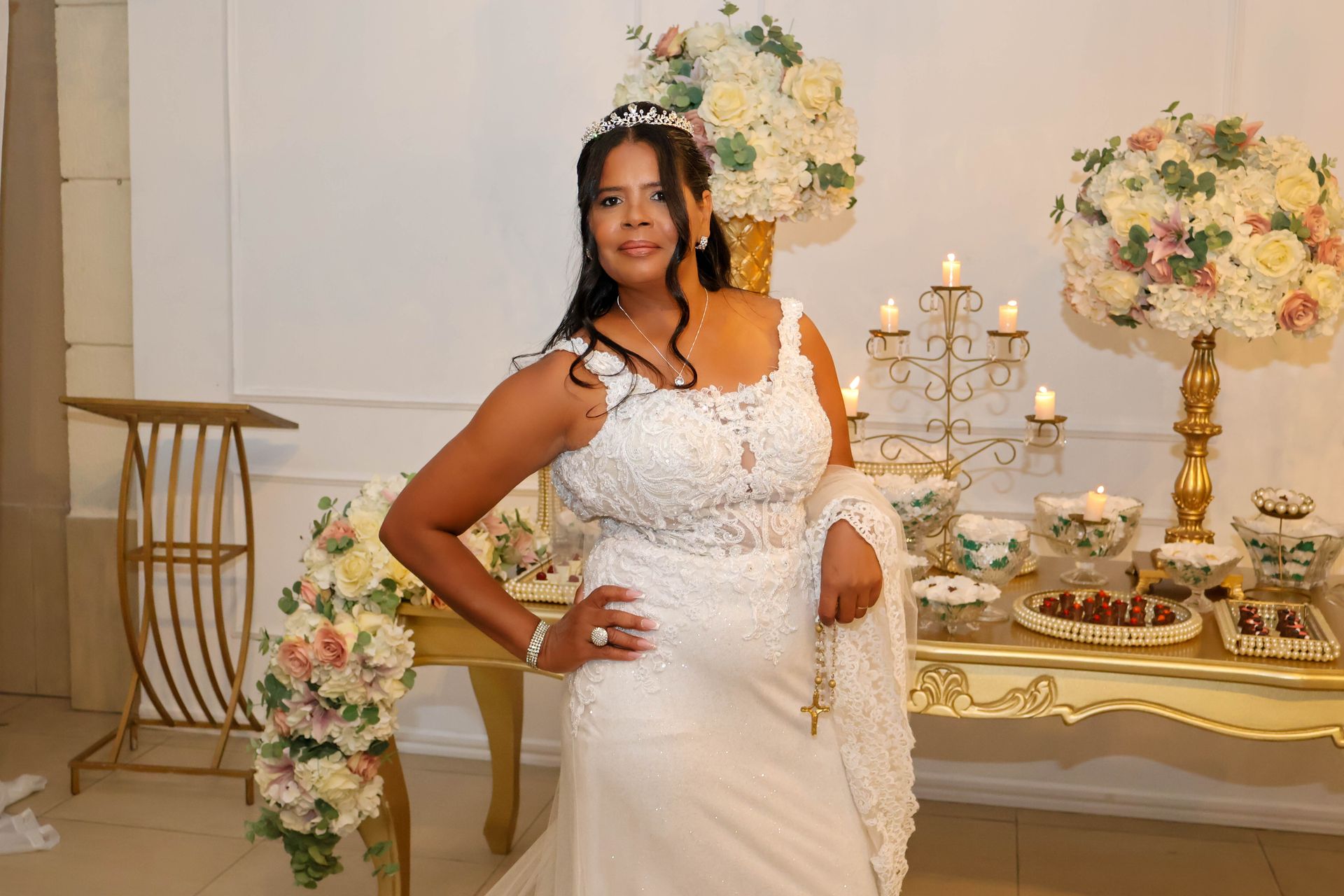 Mulher em vestido de noiva branco posa em uma mesa decorada com flores e um candelabro.