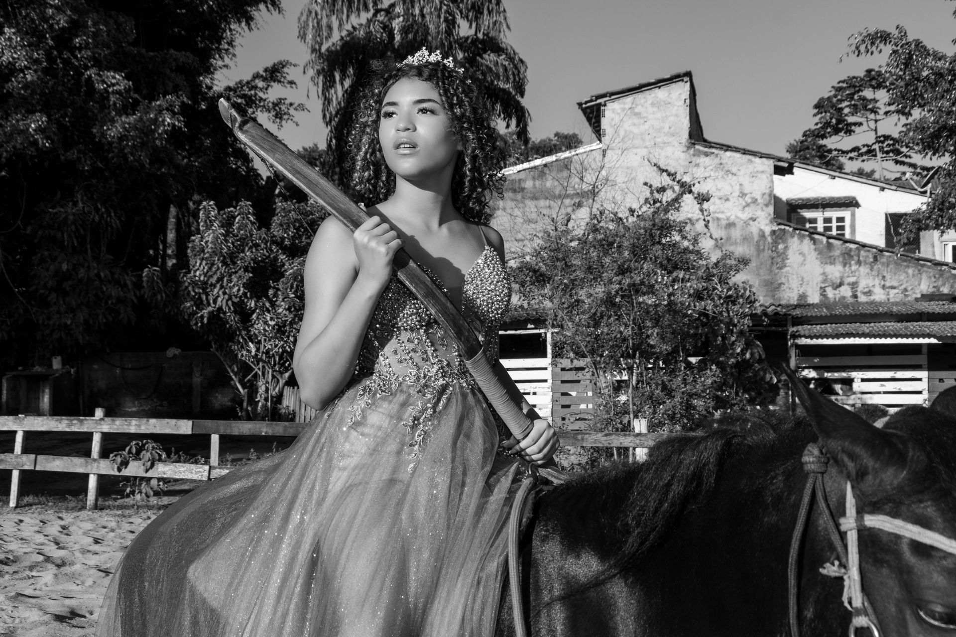 Mulher com vestido ornamentado a cavalo, segurando um arco, ao ar livre.