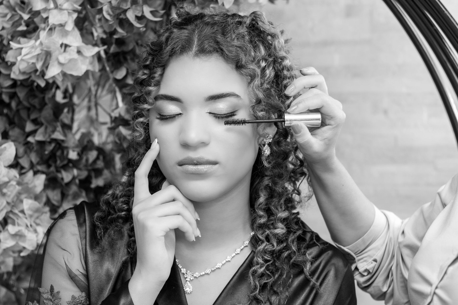 Mulher com rímel aplicado, em ambiente fechado. Ela tem cabelos cacheados, olhos fechados e usa um colar.