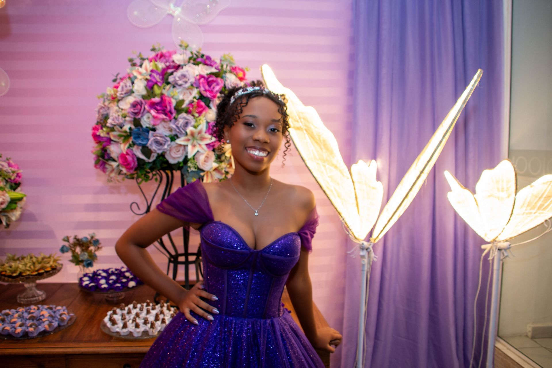 Mulher com vestido roxo brilhante em festa com decoração de flores.