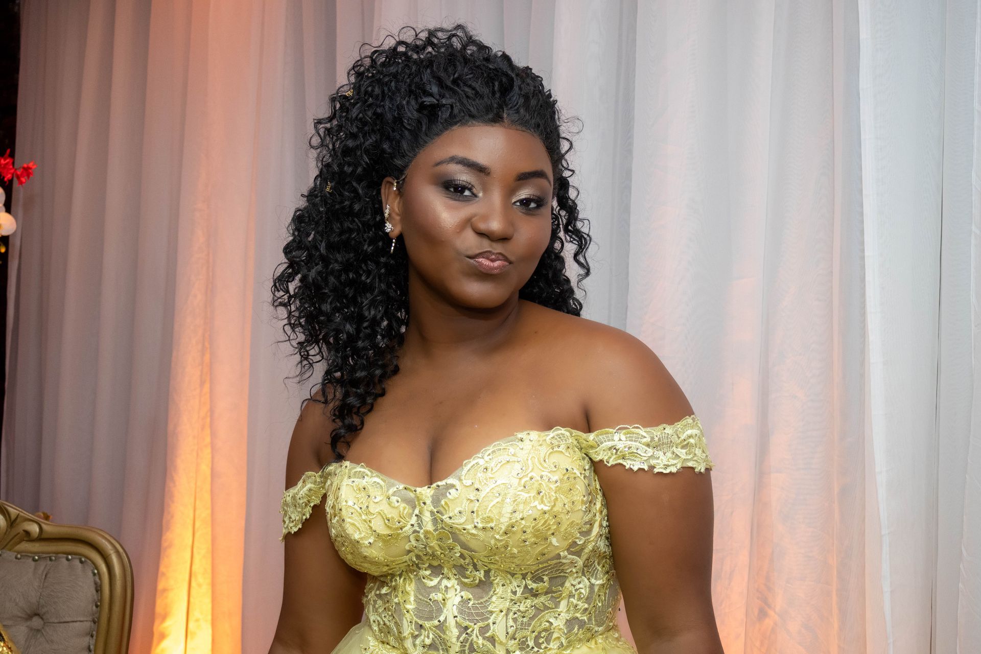 Mulher com um vestido amarelo tomara que caia posa em frente a um cenário drapeado, olhando para a câmera.