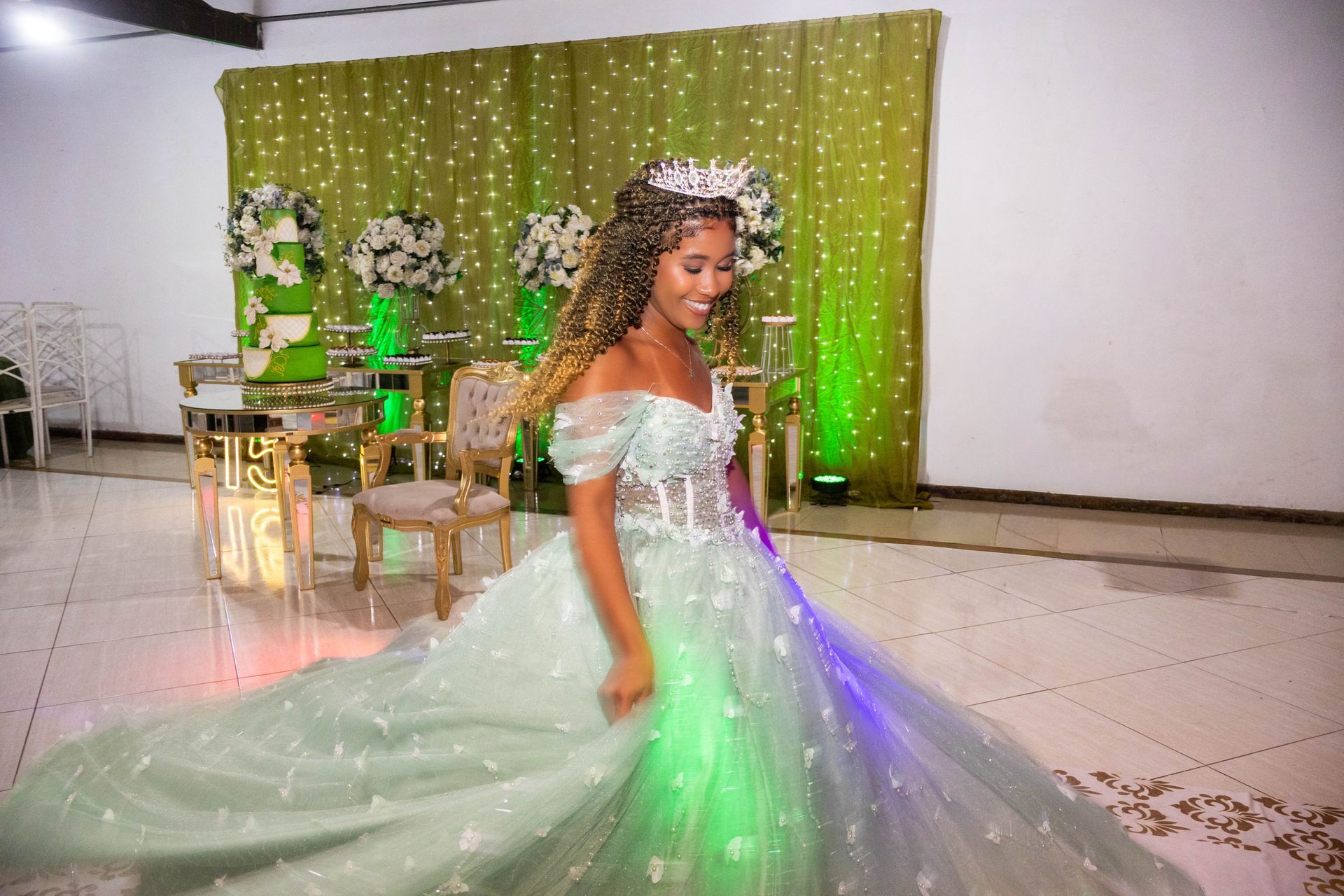 Mulher com um vestido verde claro, sorrindo, girando em uma celebração, com decorações verdes e douradas.