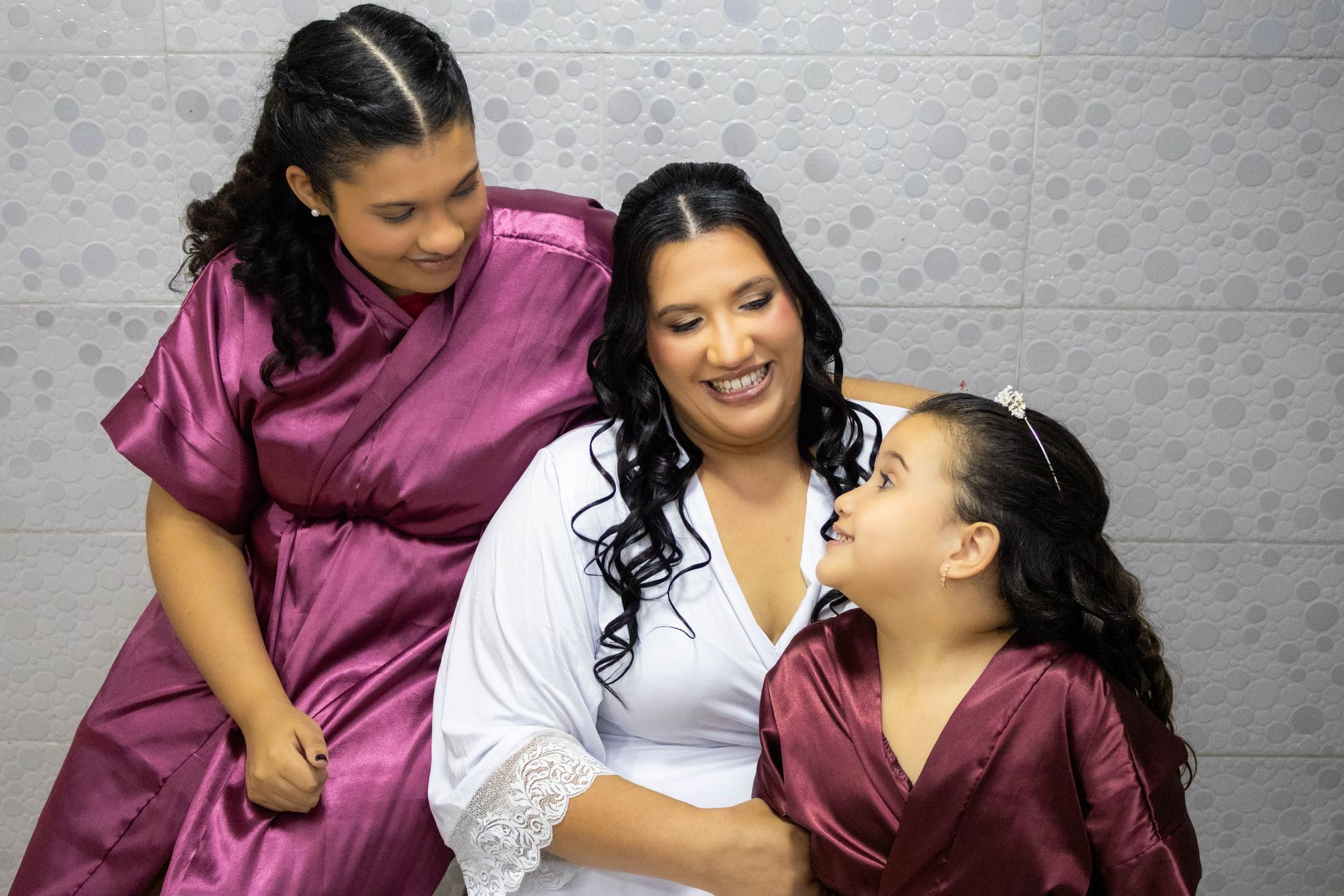 Mulher sorri com duas meninas, todas de roupão.