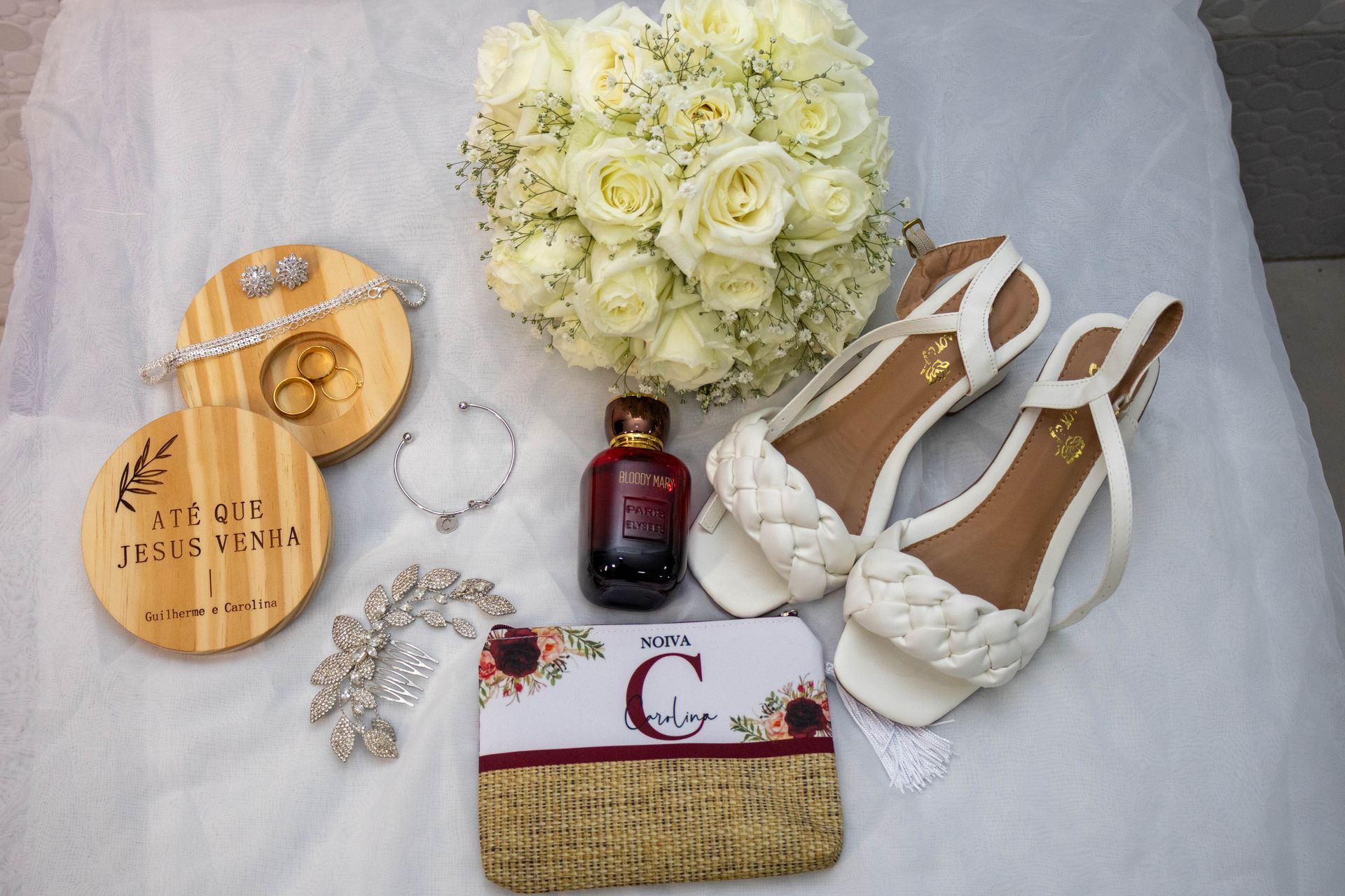 Detalhes do casamento: buquê, sapatos, joias, perfume, porta-alianças e bolsa em tecido branco.