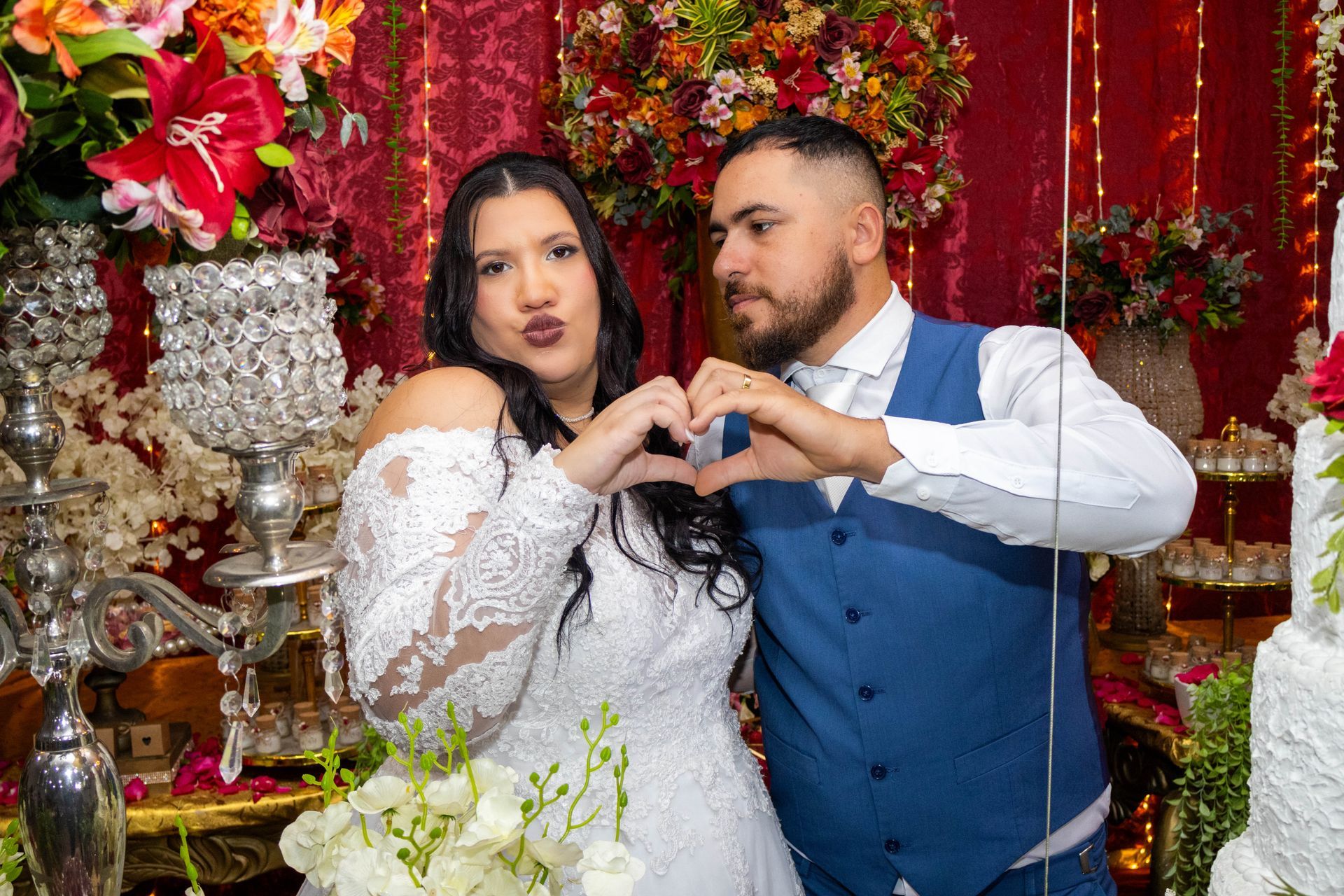 Noivos formando um coração com as mãos em um casamento. Decorações festivas ao fundo.
