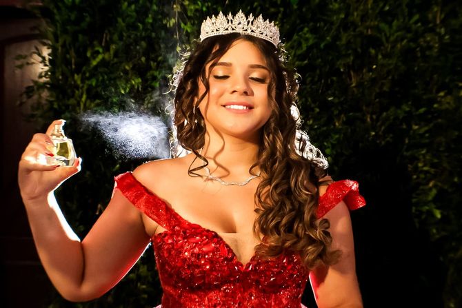 Mulher de vestido vermelho e tiara borrifa perfume.