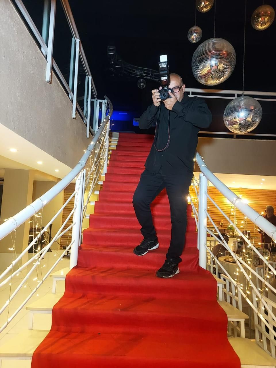 Fotógrafo em uma escada com carpete vermelho, tirando uma foto com uma câmera e flash.