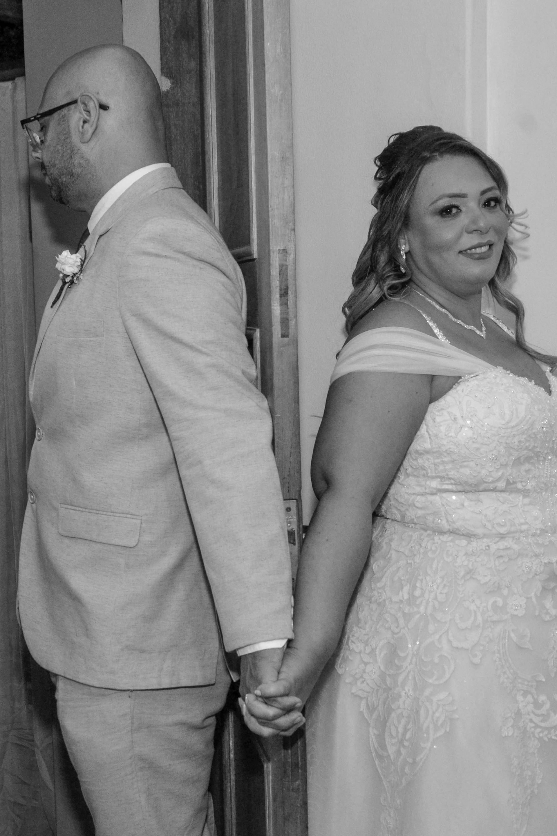 Noivos de mãos dadas, costas com costas, antes do casamento. Noiva de vestido, noivo de terno.