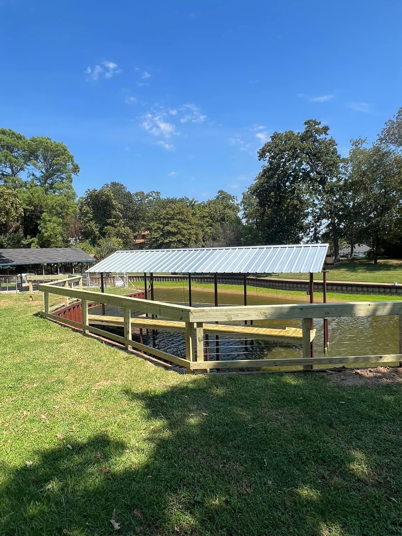 A wooden dock with a metal roof is sitting next to a body of water.