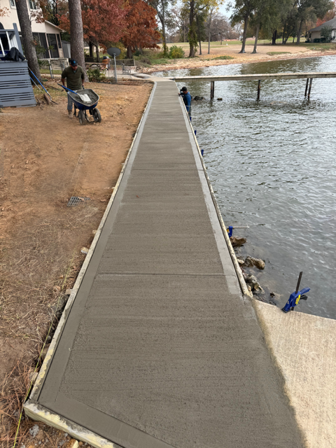 A man is pushing a wheelbarrow down a dock next to a body of water.