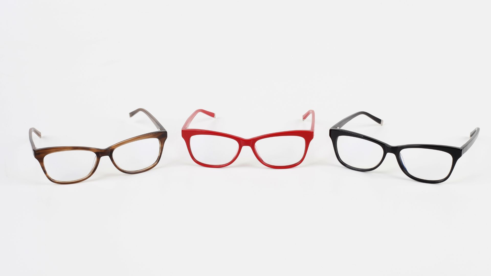 Three pairs of eyeglasses in brown, red, and black frames, arranged horizontally against a white background.