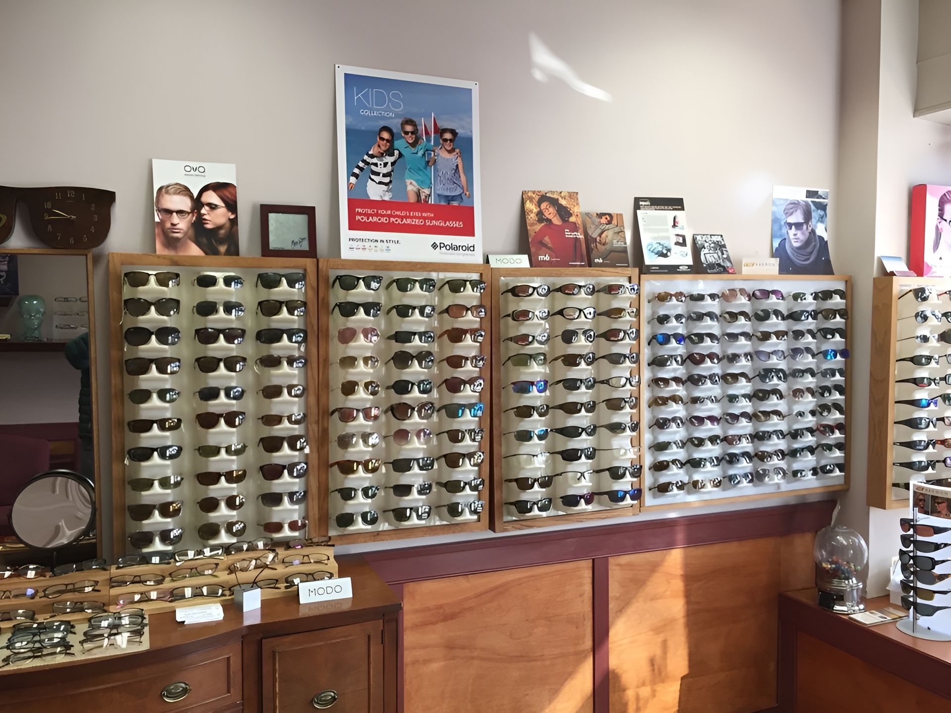 Two young children with sunglasses and denim jackets pose against a yellow background. The boy has his arm around the girl.