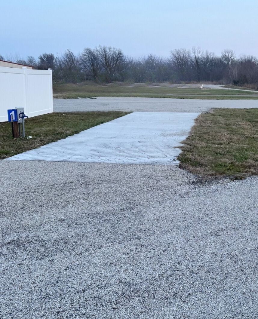RV campsite level pad with concrete Gravel RV campsite with newly poured concrete pad and numbered hookups at Downey Carriage House RV Park surrounded by trees