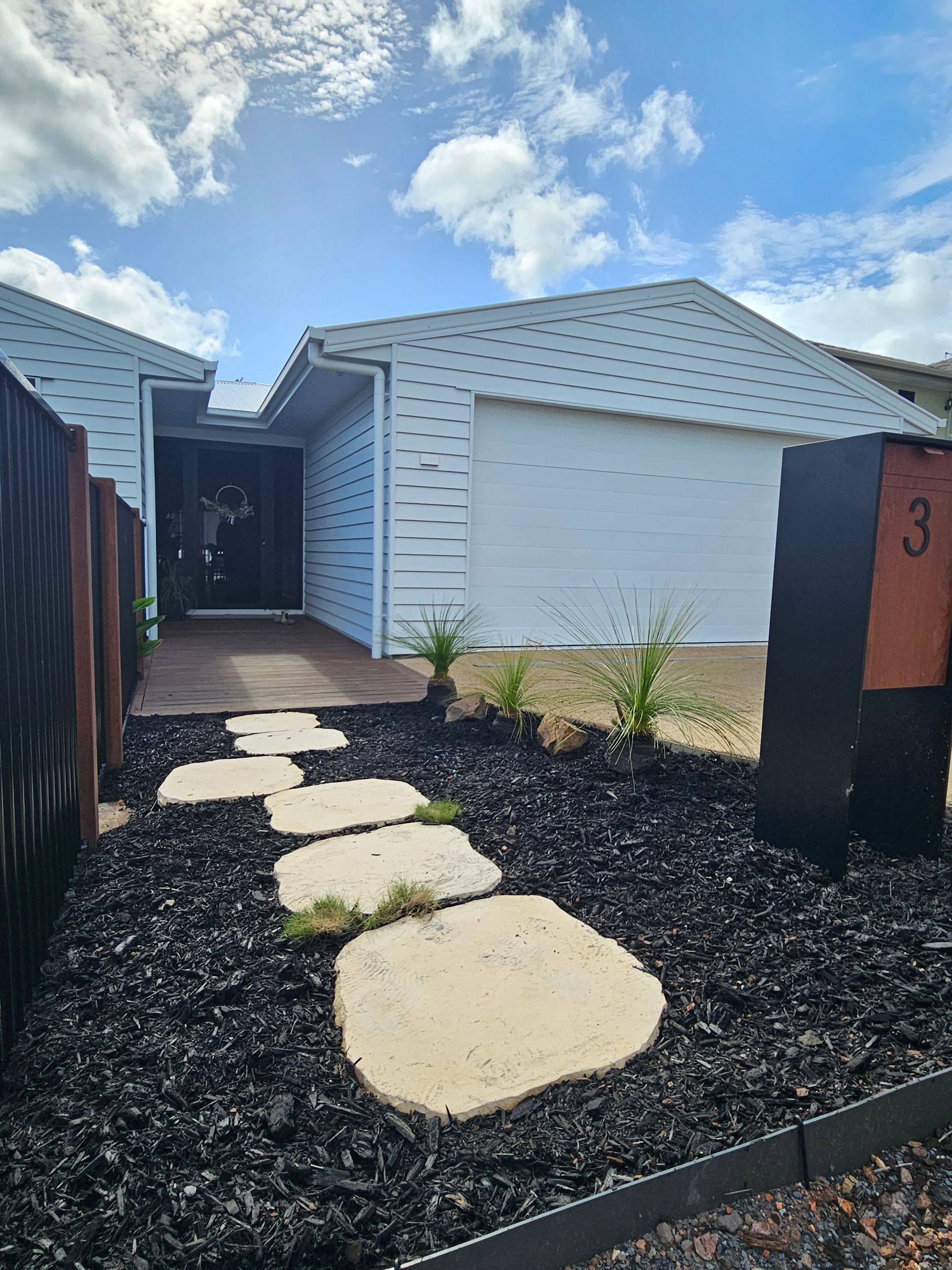 A white house with a modern patterned exterior, black mulch garden, stepping stones, and a metal mailbox labeled 3.