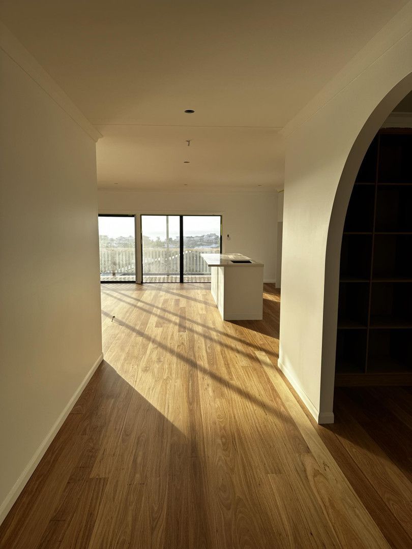 A hallway with light wood floors leads into a bright room with a kitchen island and large windows overlooking a balcony.