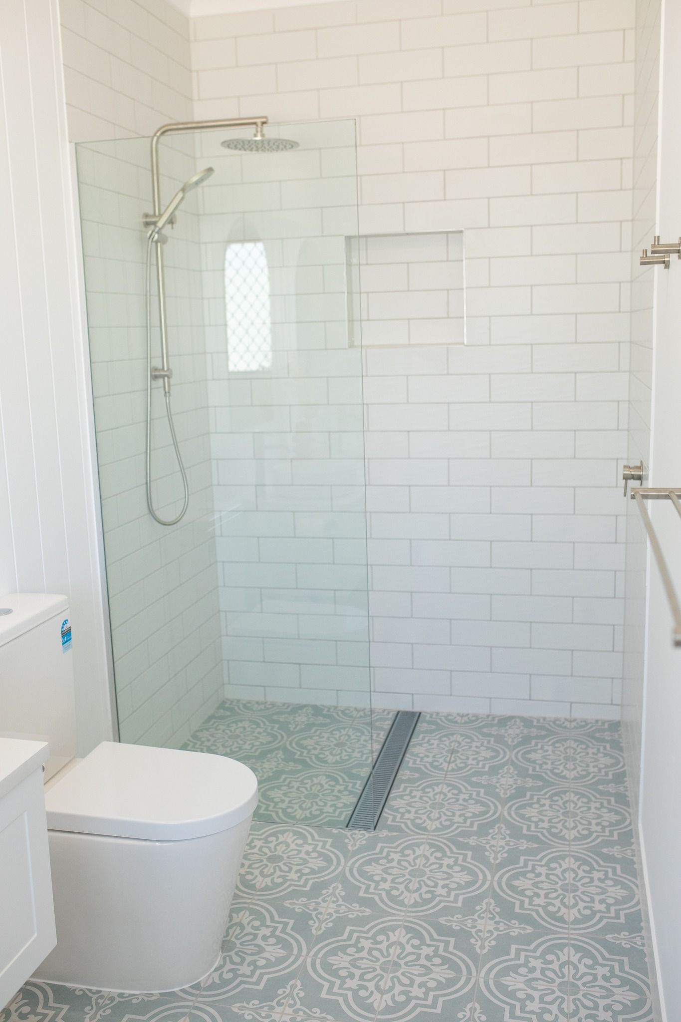 A modern bathroom with white subway tile walls, a glass-enclosed shower, patterned floor tiles, and a white toilet — Jones Building Group in Yeppoon, QLD