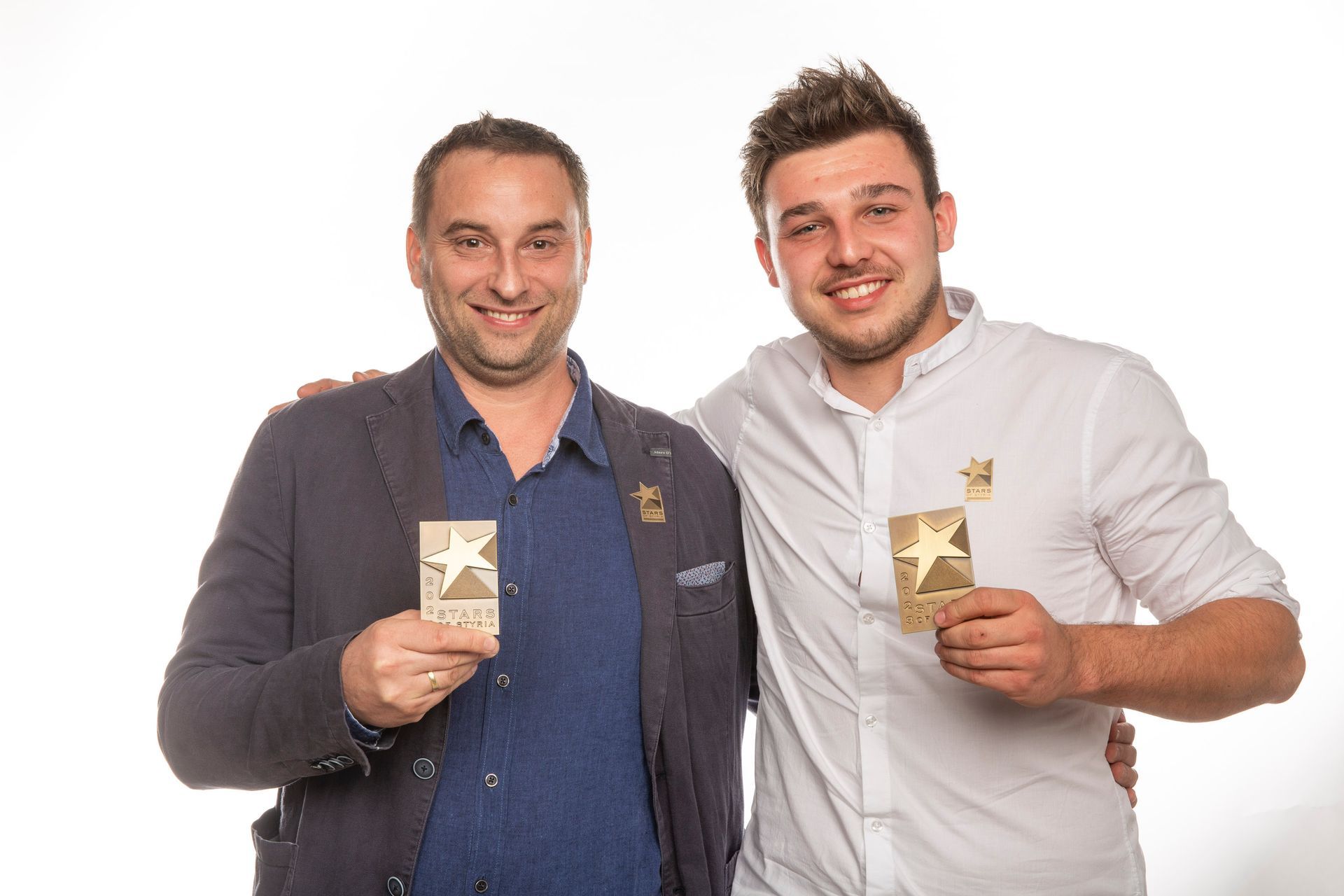 Zwei Männer stehen nebeneinander und halten Auszeichnungen in den Händen.