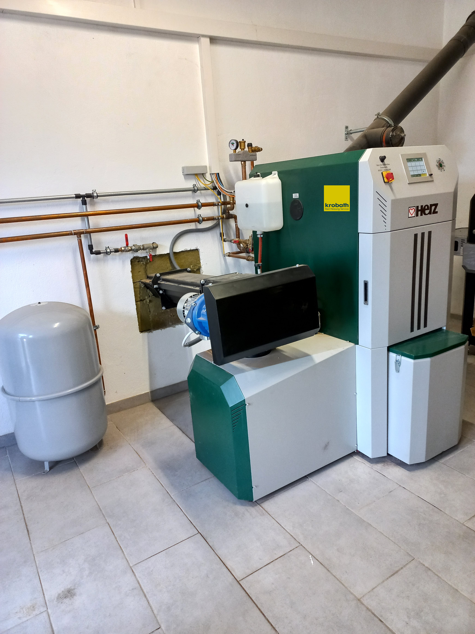 Eine grün-weiße Maschine steht in einem Raum neben einem grauen Tank.