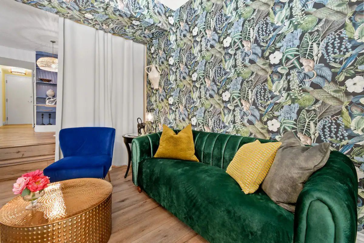 A living room with a green couch , blue chairs , and a gold coffee table.