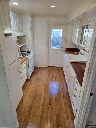 A kitchen with hardwood floors , white cabinets , a stove and a refrigerator.