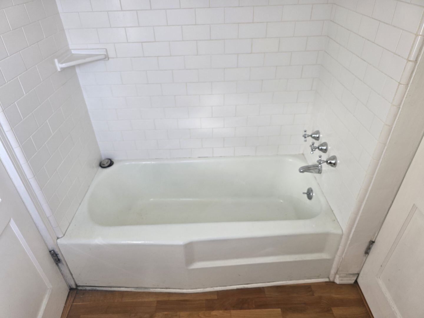 A white bathtub in a bathroom with white tiles.
