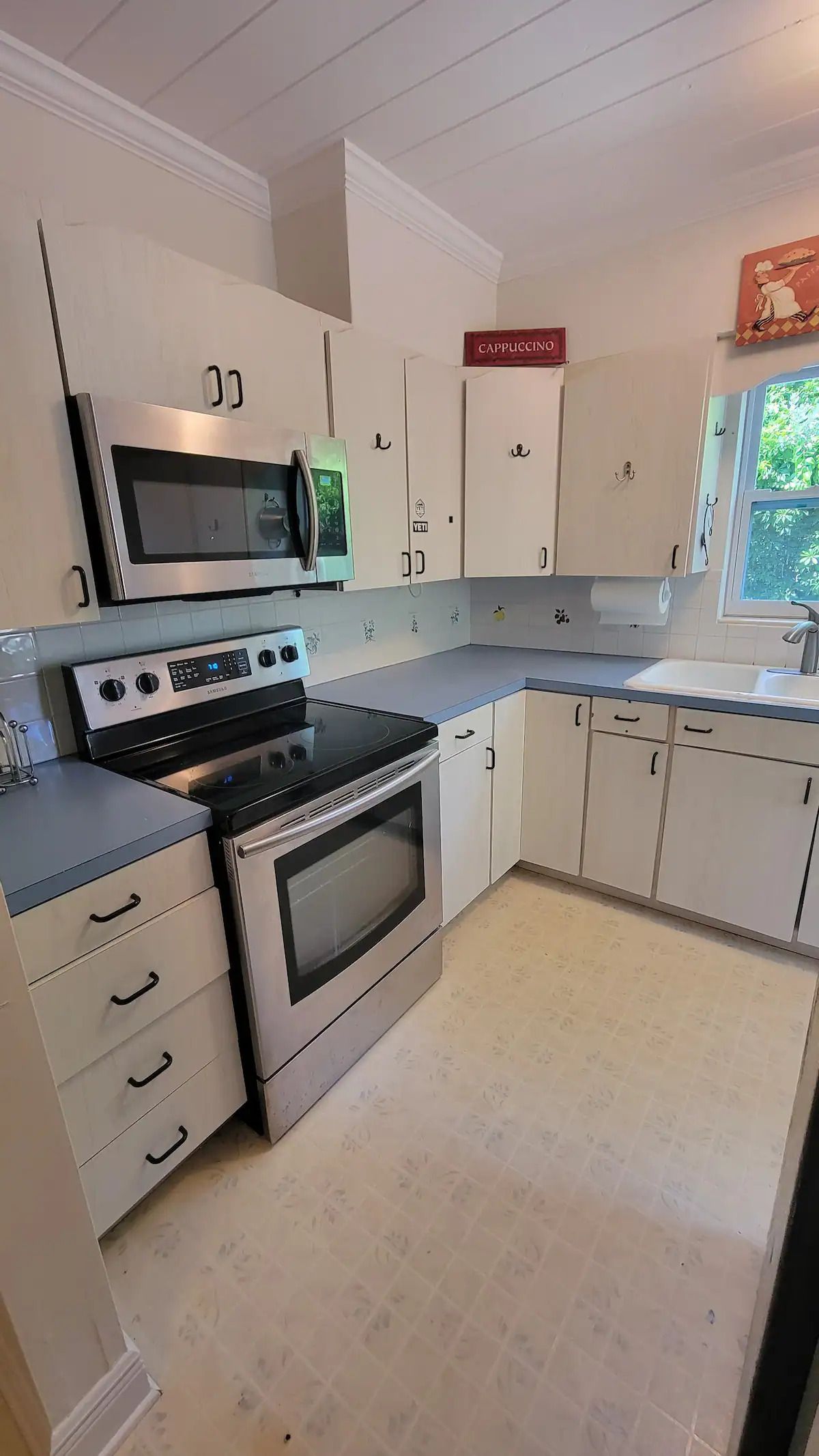 A kitchen with white cabinets , a stove , a microwave , and a sink.