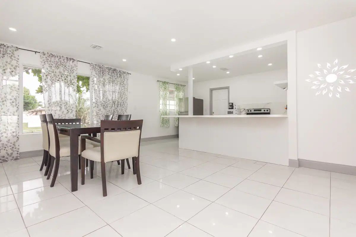 A dining room with a table and chairs and a kitchen in the background.