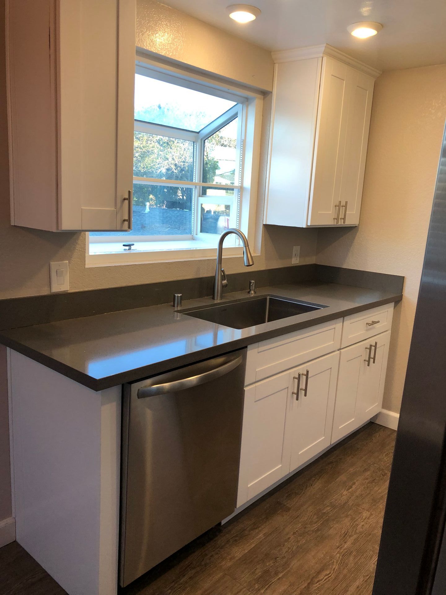 A kitchen with white cabinets , stainless steel appliances , a sink and a window.