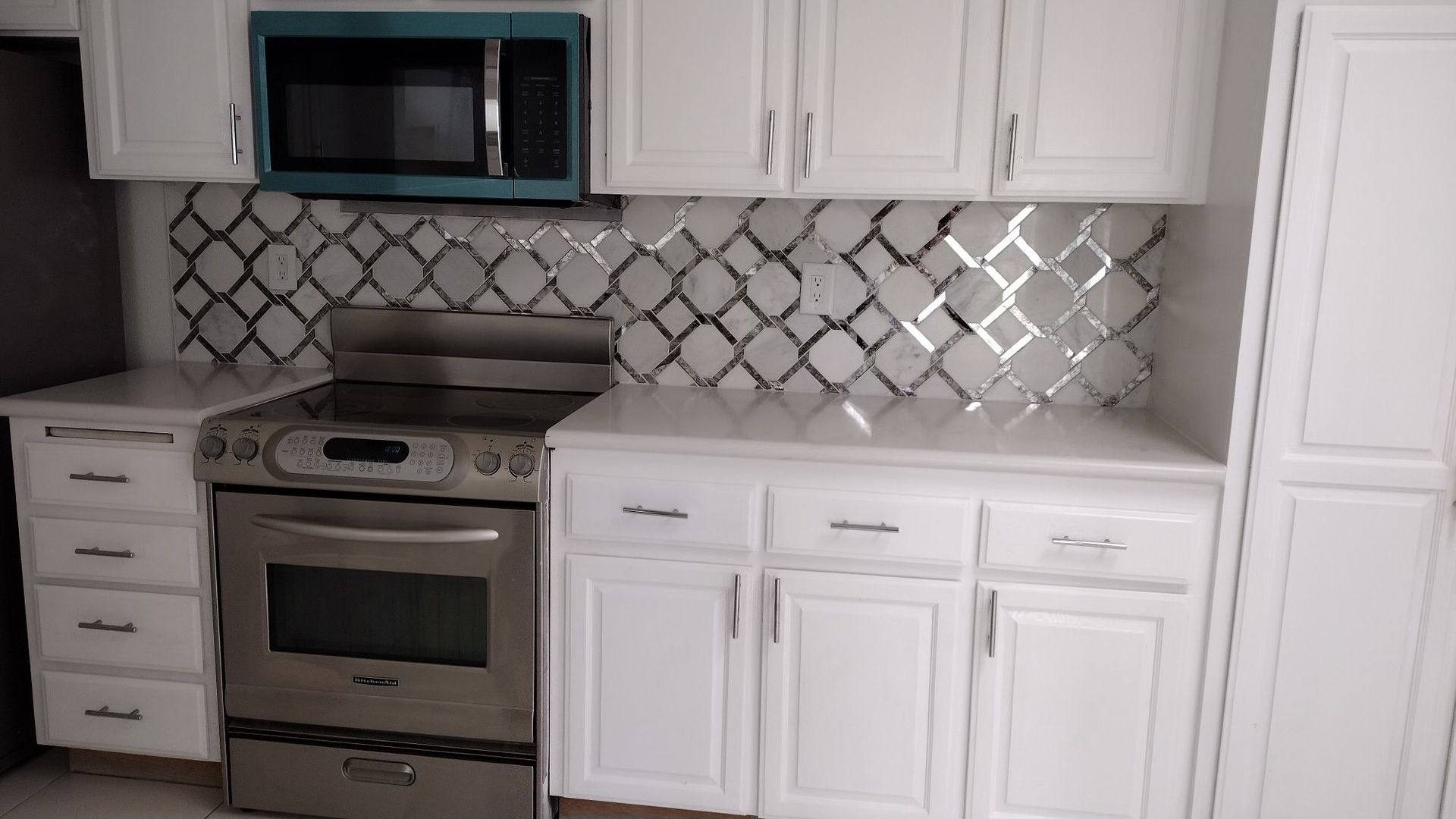 A kitchen with white cabinets , a stove , a microwave , and a refrigerator.