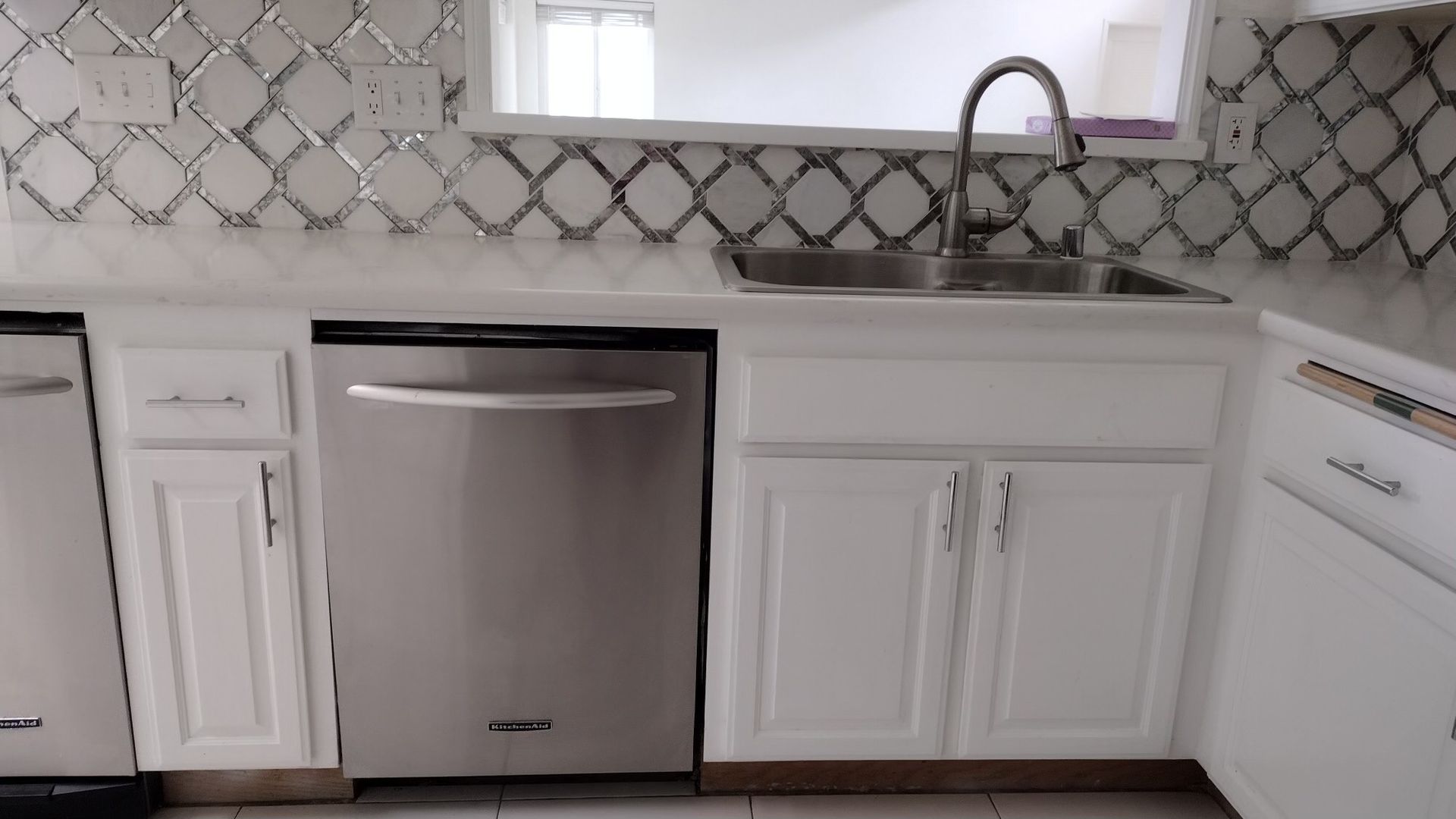 A kitchen with white cabinets , stainless steel appliances , a sink and a dishwasher.