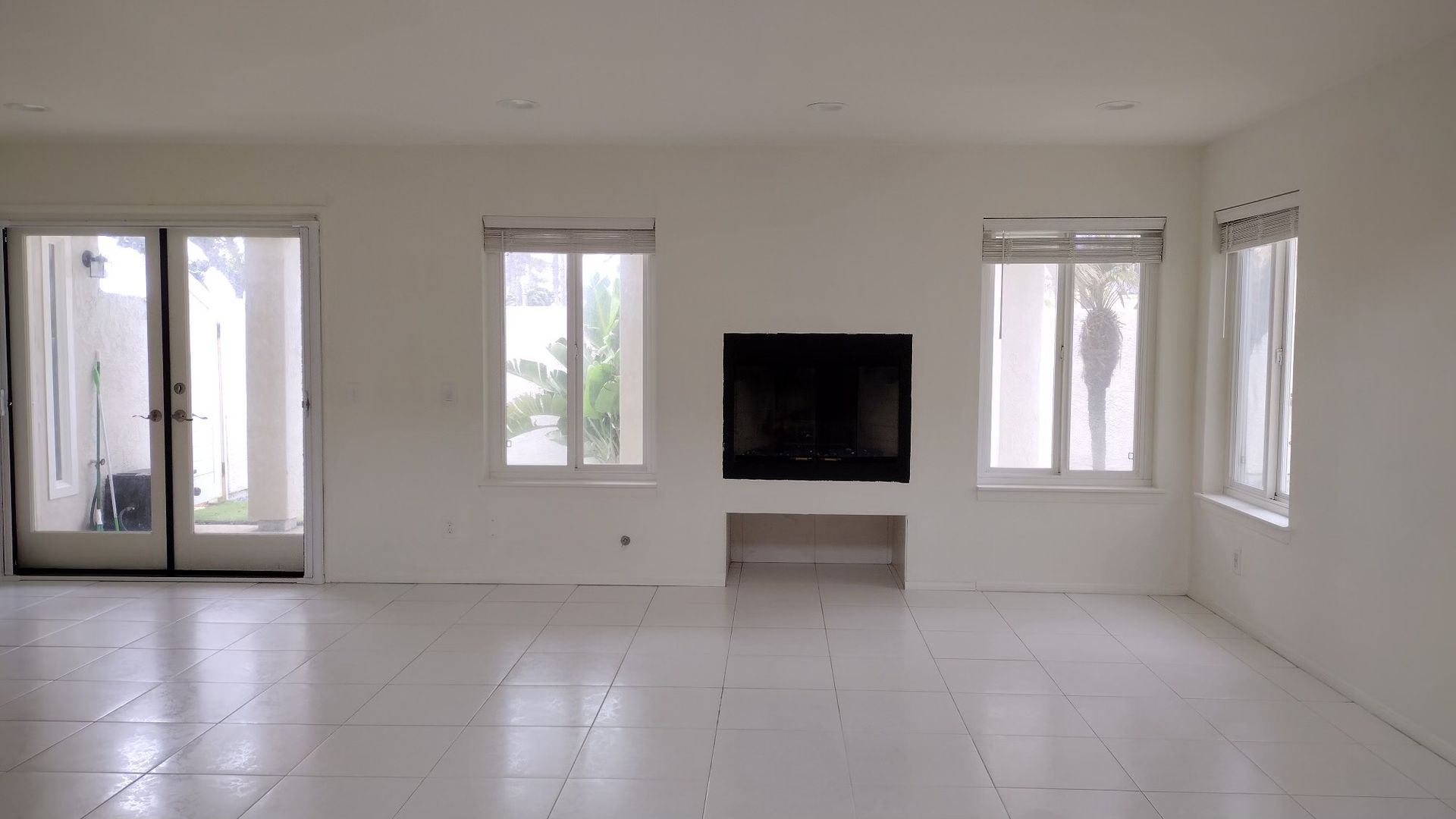An empty living room with white tile floors and a fireplace.