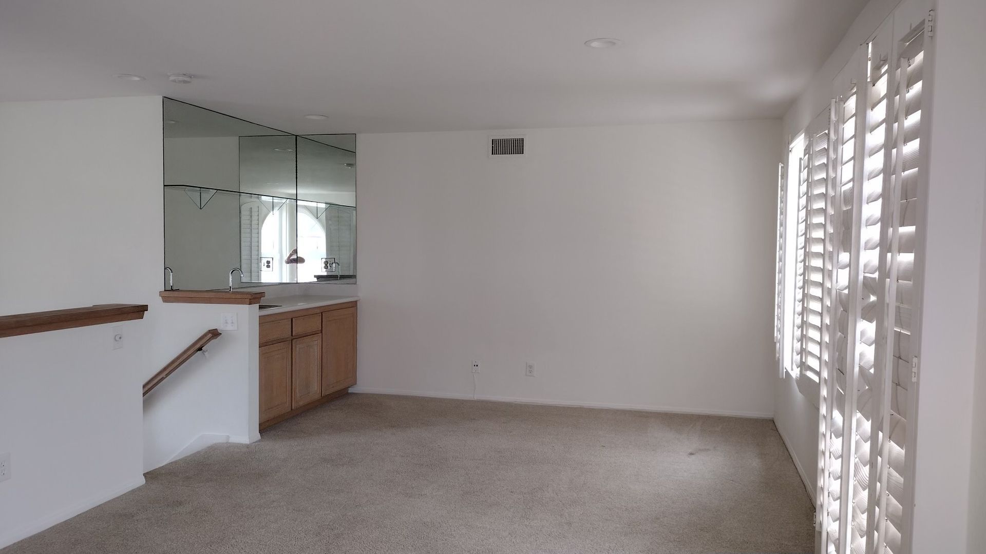 An empty living room with a staircase and shutters on the windows.
