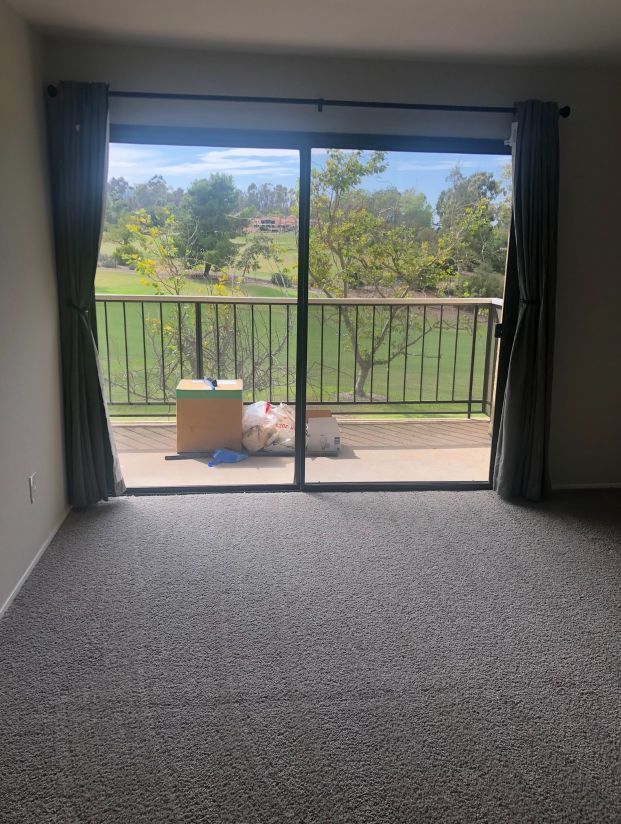 An empty living room with a sliding glass door leading to a balcony.