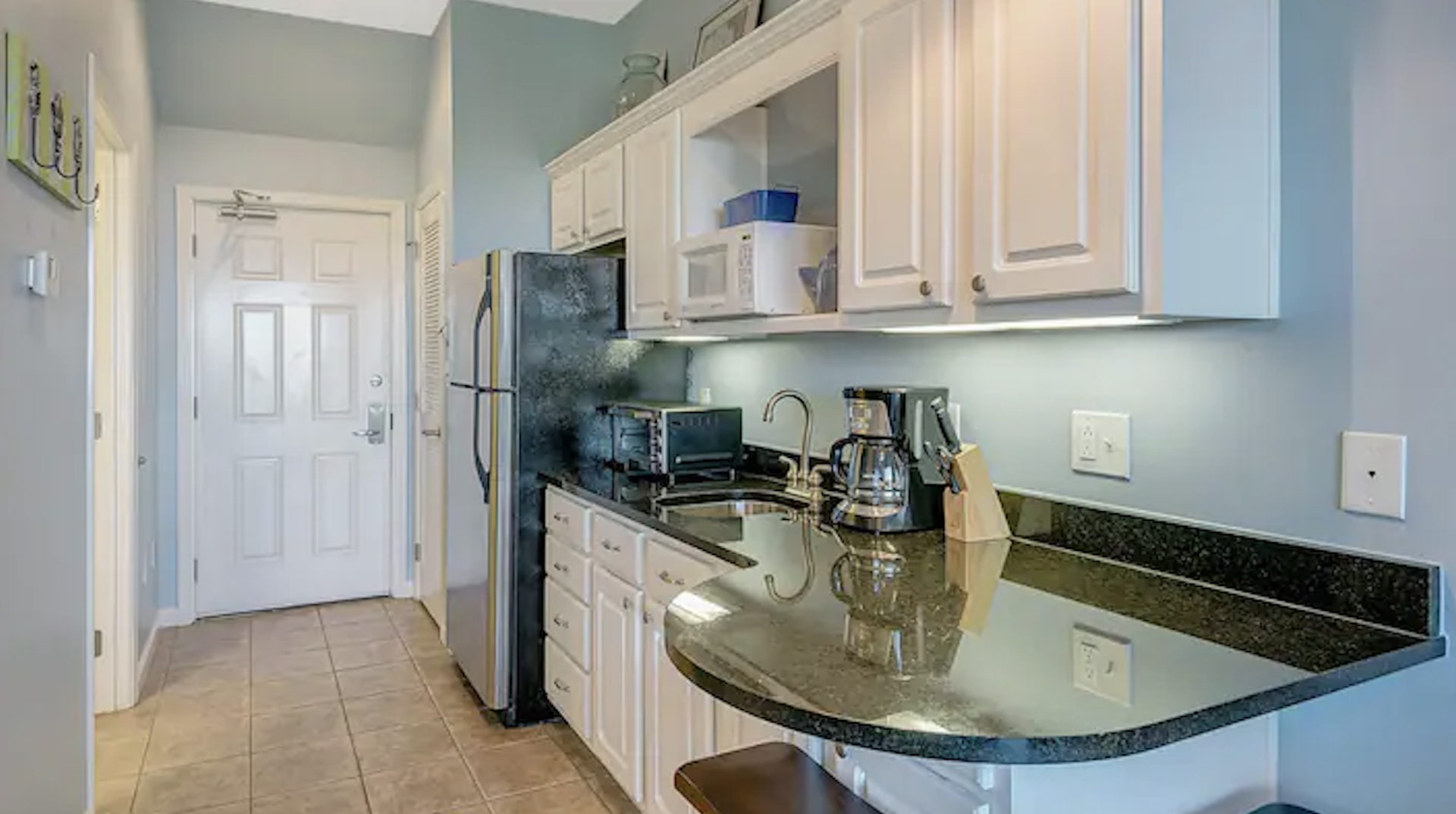 A kitchen with white cabinets , granite counter tops , stainless steel appliances and a refrigerator.