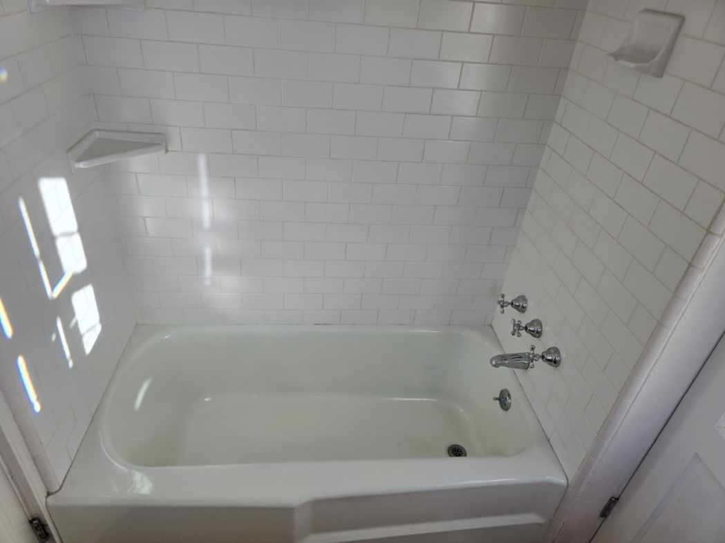 There is a bathtub in the bathroom with white tiles.