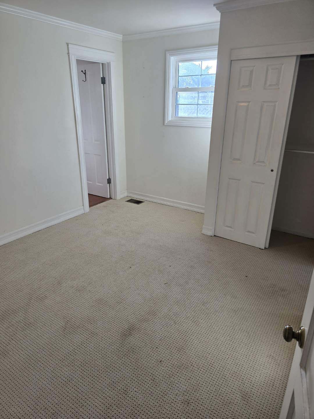 An empty bedroom with a closet and a window.