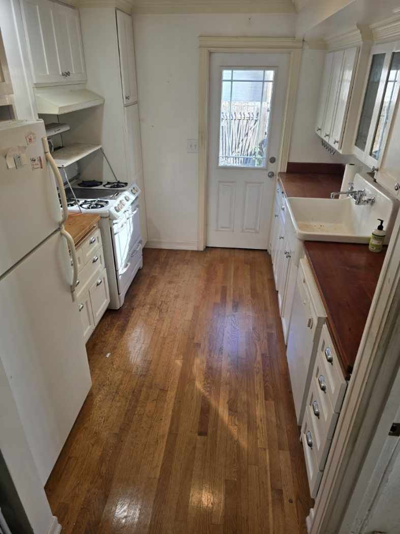 A kitchen with hardwood floors , white cabinets , a refrigerator , stove and sink.