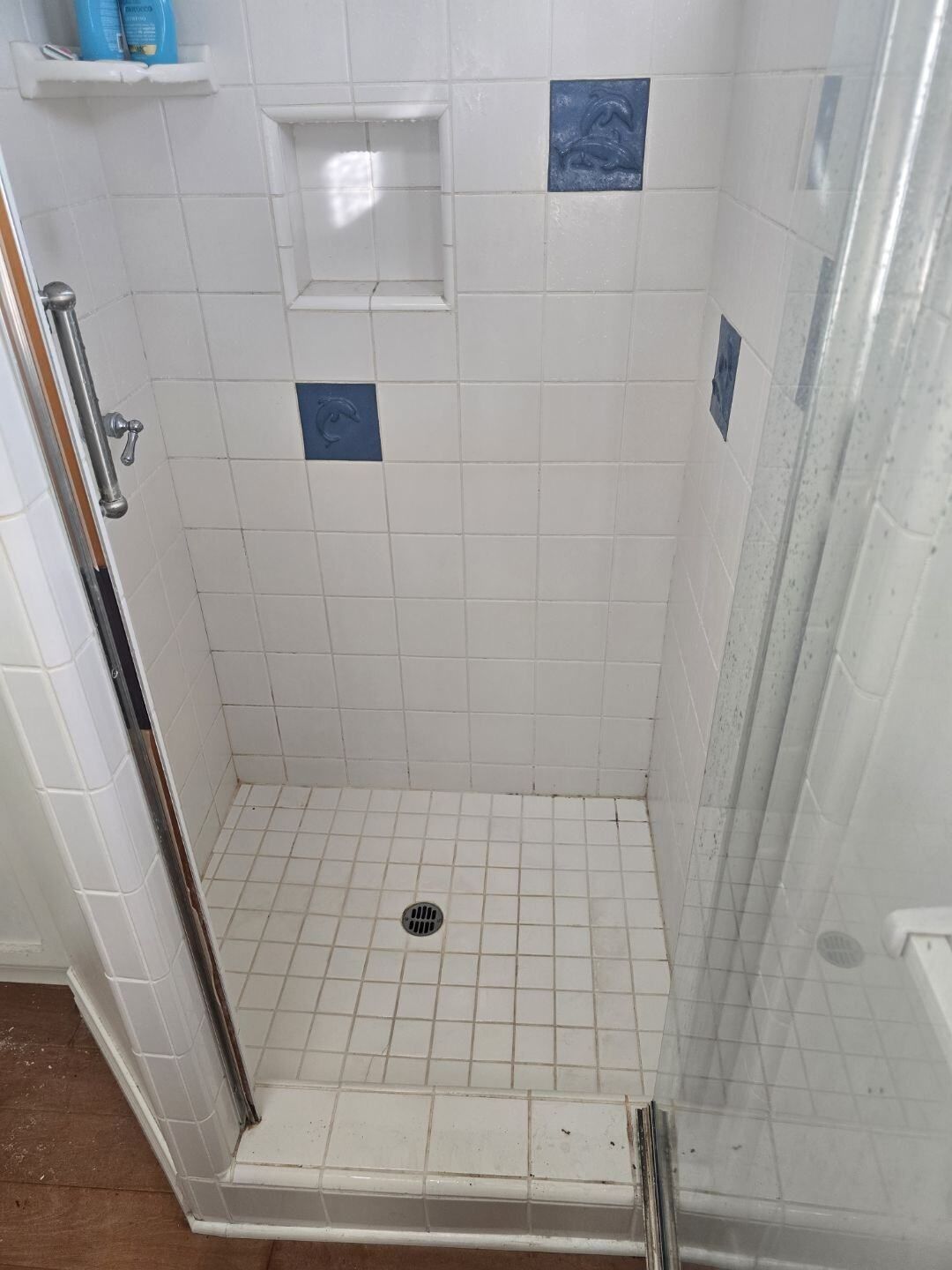A shower stall with a glass door and white tiles in a bathroom.