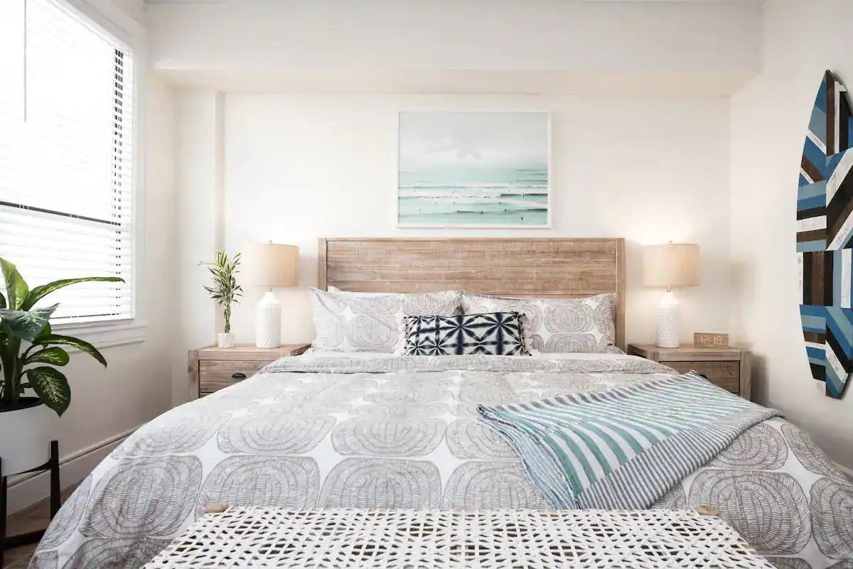 A bedroom with a bed , nightstands , lamps and a painting on the wall.