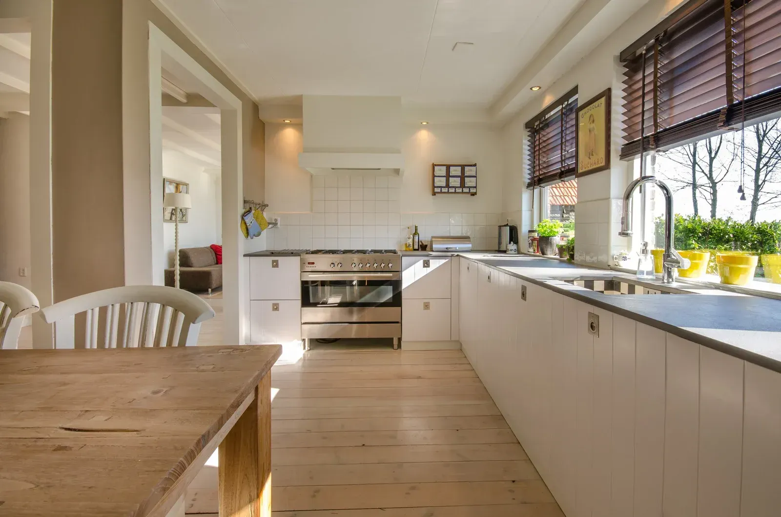Bright, modern kitchen with white cabinets, wood floors, and a window with blinds.