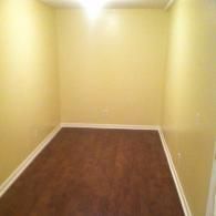 Empty room with pale yellow walls, white baseboards, and dark brown wood-look flooring.
