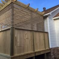 A wooden deck with a high privacy screen featuring horizontal slats above and vertical slats below, attached to a house.
