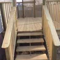 A set of wooden stairs with railings leading up to a wooden deck with a privacy lattice screen.