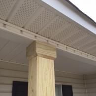 A wooden porch post topped with a decorative cap under the soffit of a home with light-colored vinyl siding.